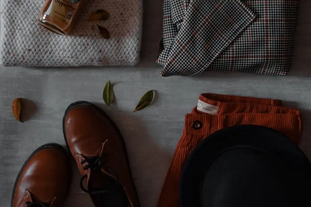 Flat lay of brown shoes, sweater, plaid scarf, pants and hat on grey background - fashion style inspiration