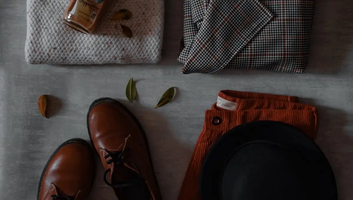 Flat lay of brown shoes, sweater, plaid scarf, pants and hat on grey background - fashion style inspiration