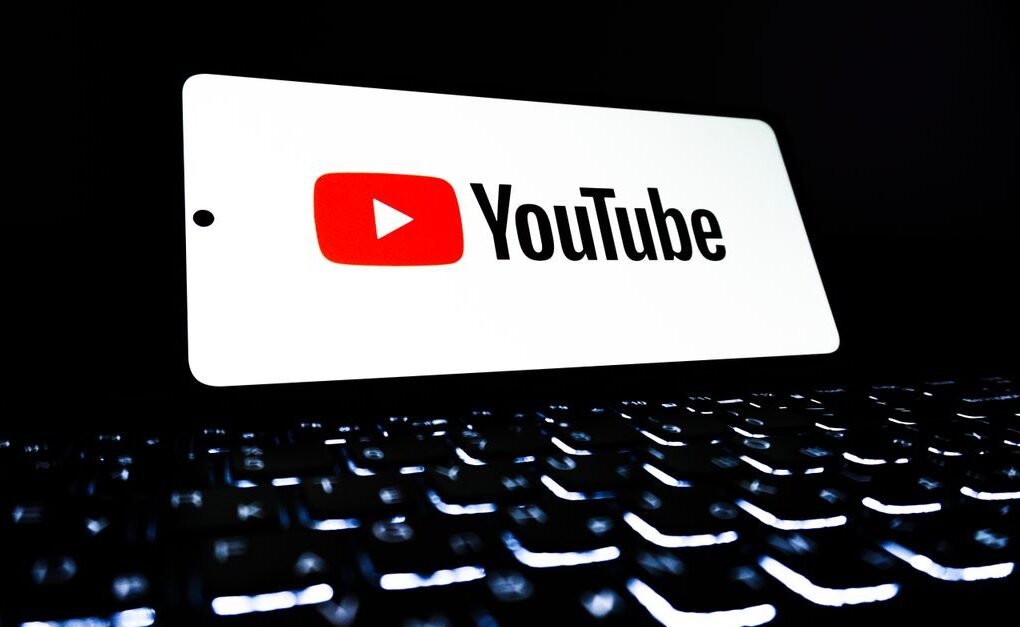 YouTube app icon displayed on a smartphone over an illuminated keyboard, representing digital media and online streaming.